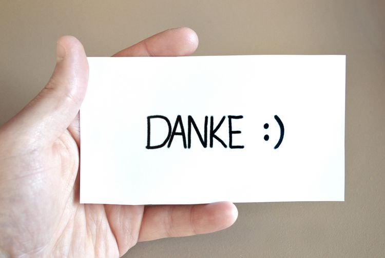 Eine Hand hält eine Karte, darauf steht "Danke" mit einem lachenden Smiley.